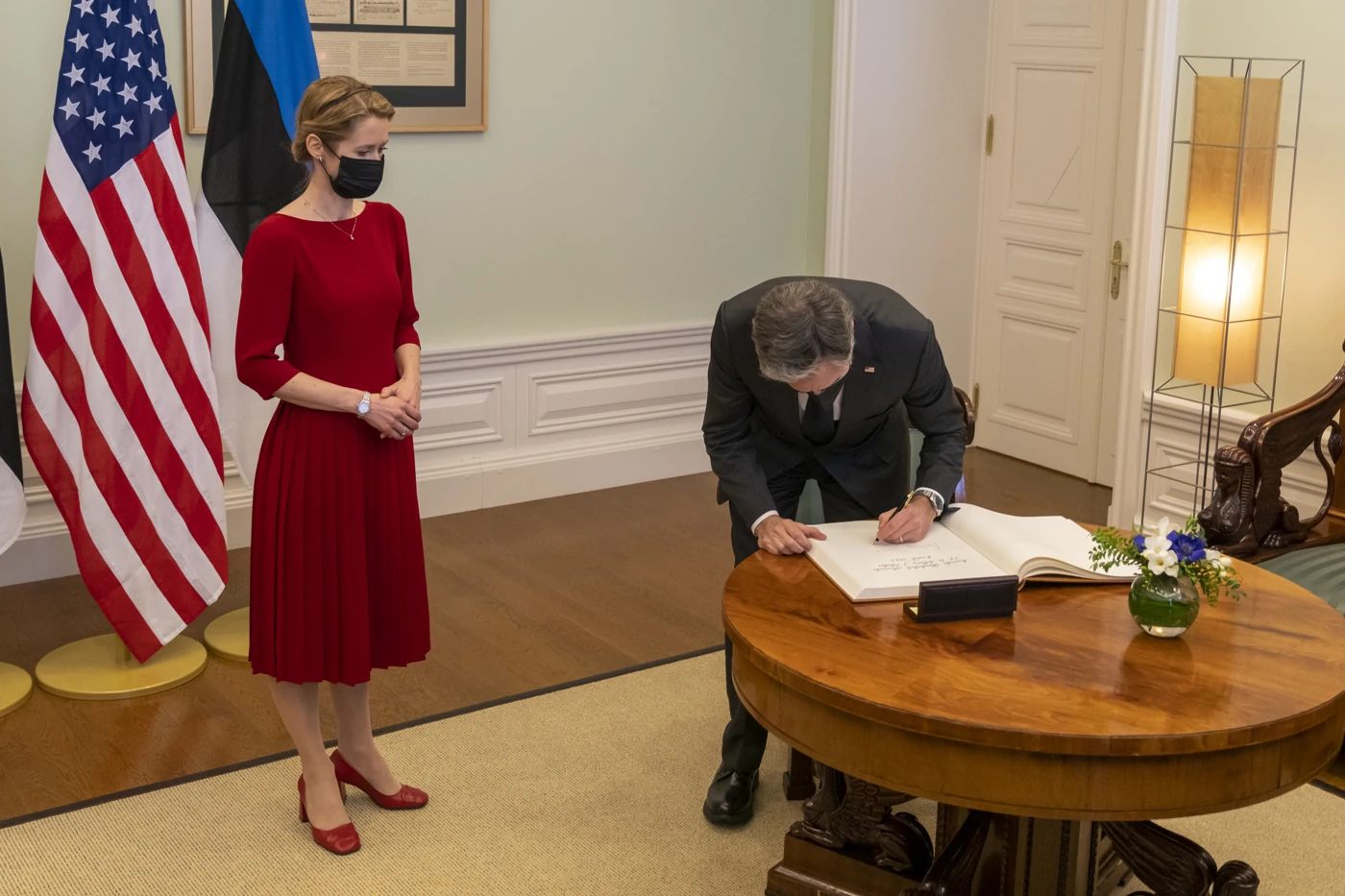 Antony Blinken signs a book beside Kaja Kallas during their meeting in Tallinn, Estonia, on March 8, 2022. Estonia’s blue-black-white flag stands behind Kallas beside the U.S. flag.