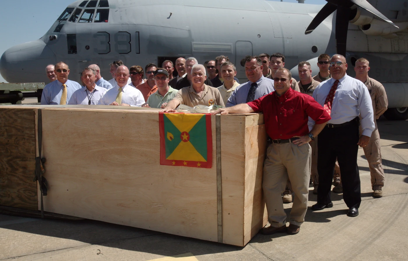 A Grenada flag hangs over a crate during a group photograph at Marine Corps Base Quantico in April 2009. The Marine Corps caption associates the crate with a helicopter component returned from Grenada.