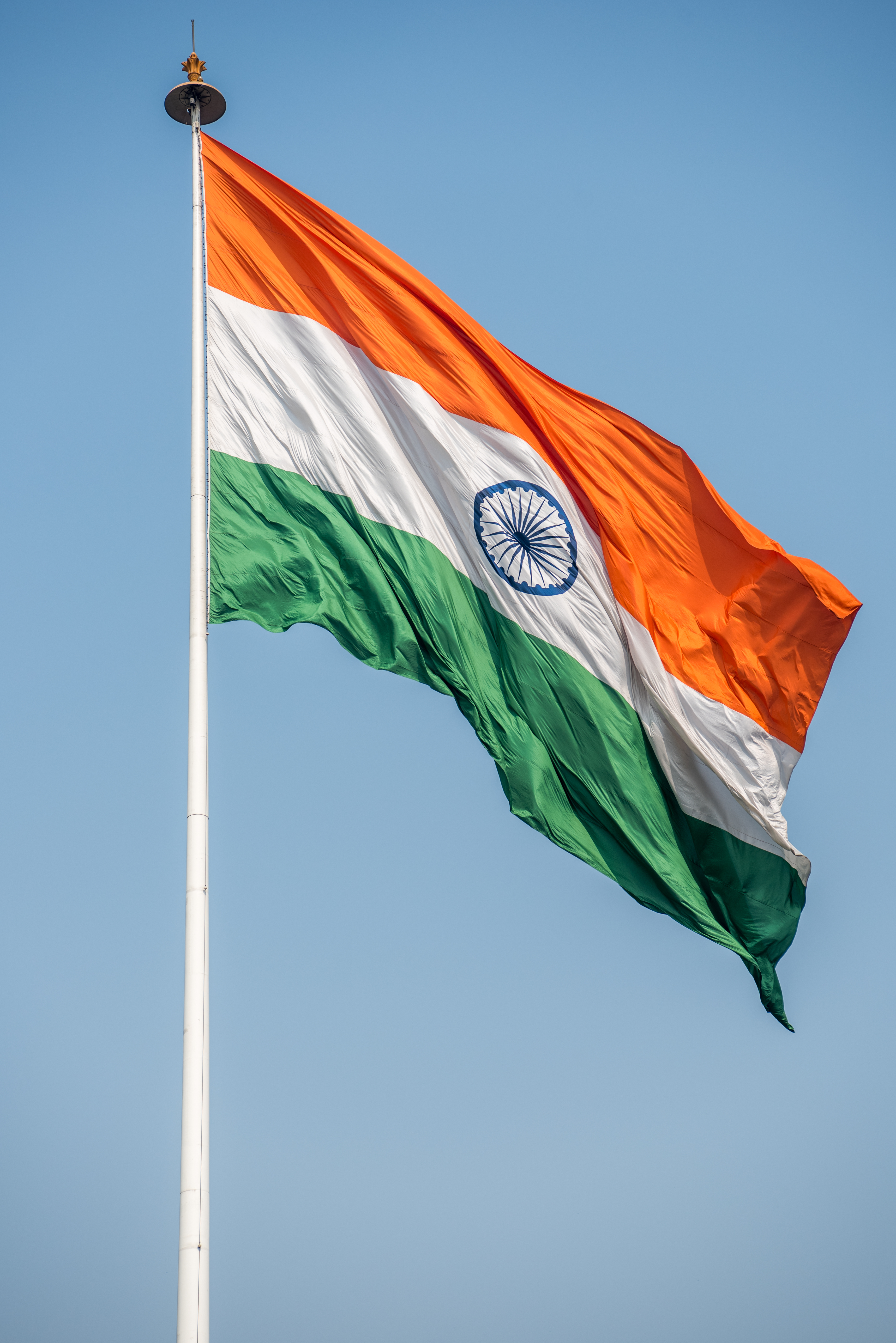 A real Indian flag draping from its pole against a clear blue sky, saffron catching the light