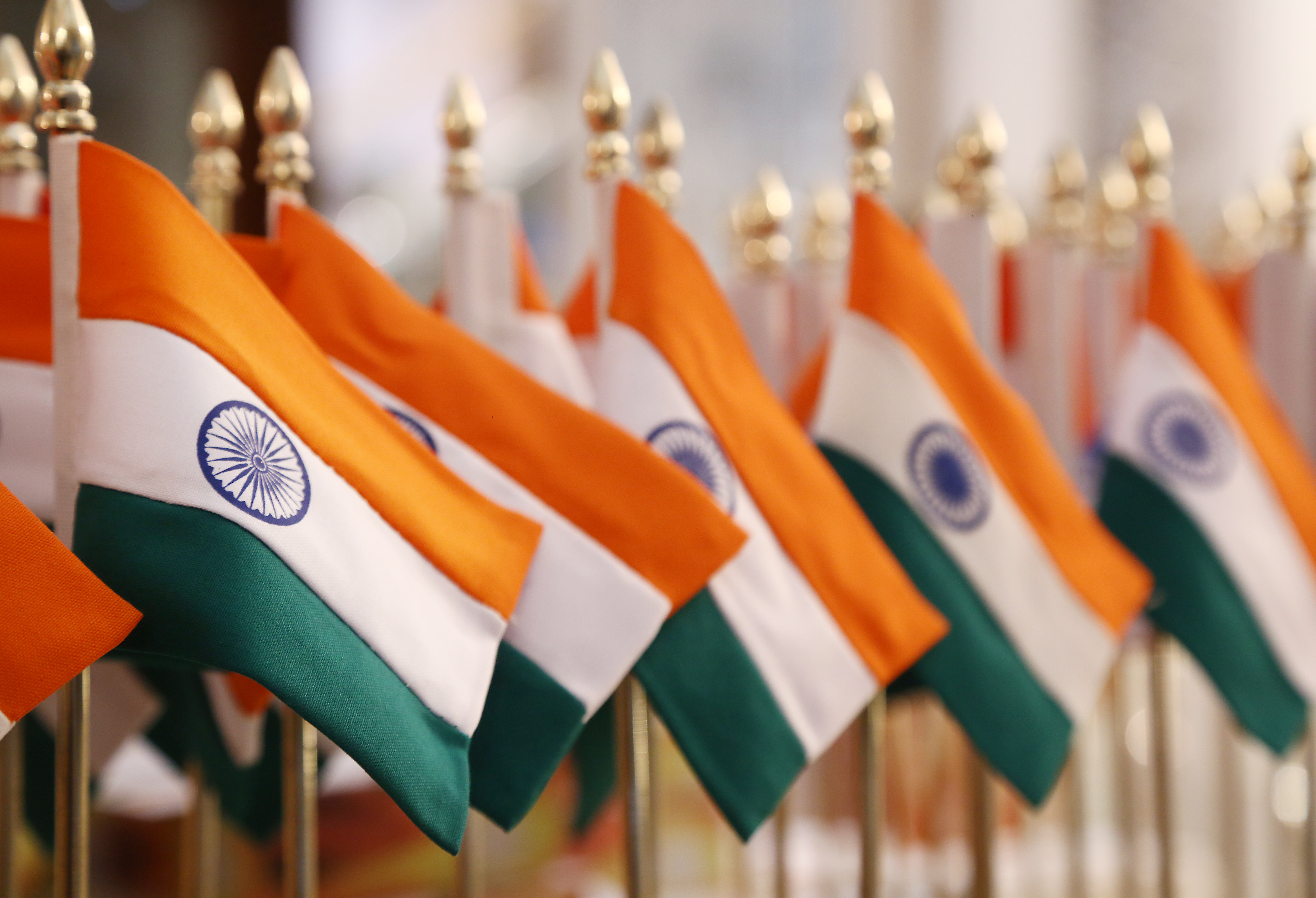 Rows of small Indian table flags on golden stands, saffron, white and green with the Ashoka Chakra, lined up in soft focus