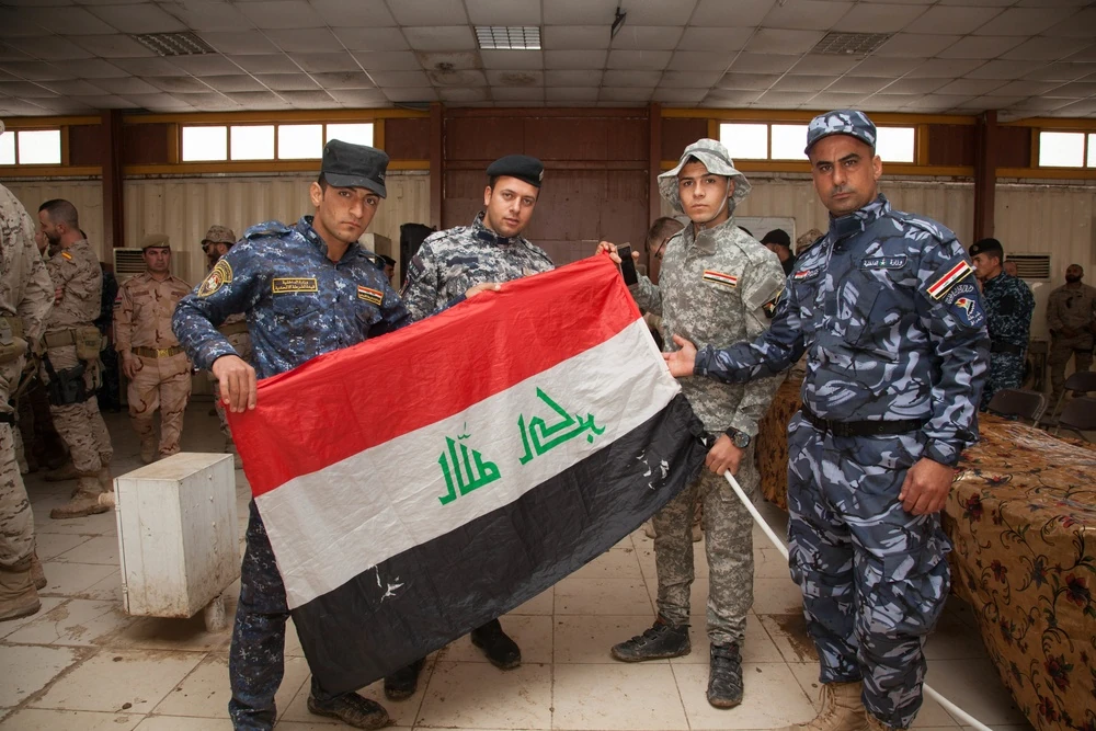 Iraqi security forces personnel hold an Iraqi flag at Besmaya Range Complex on March 23, 2017. The cloth faces the camera from its reverse, so its lettering appears mirrored.
